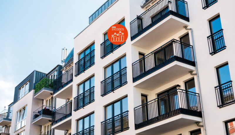 Photo d'un immeuble d'appartements récents. Logo du Dispositif SYCODÉS de l'AQC en haut