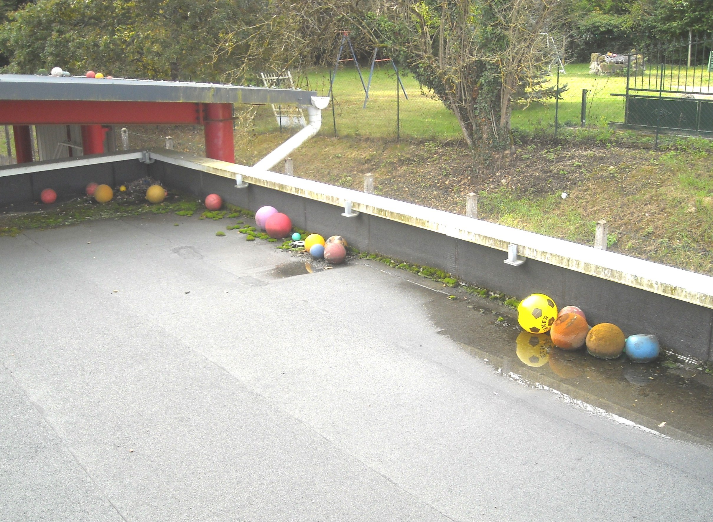 Toit d'un bâtiment scolaire jonché de feuilles d'arbres et de ballons.